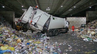 Ein Müllauto entleert den eingesammelten Verpackungsmüll in einer großen Halle.