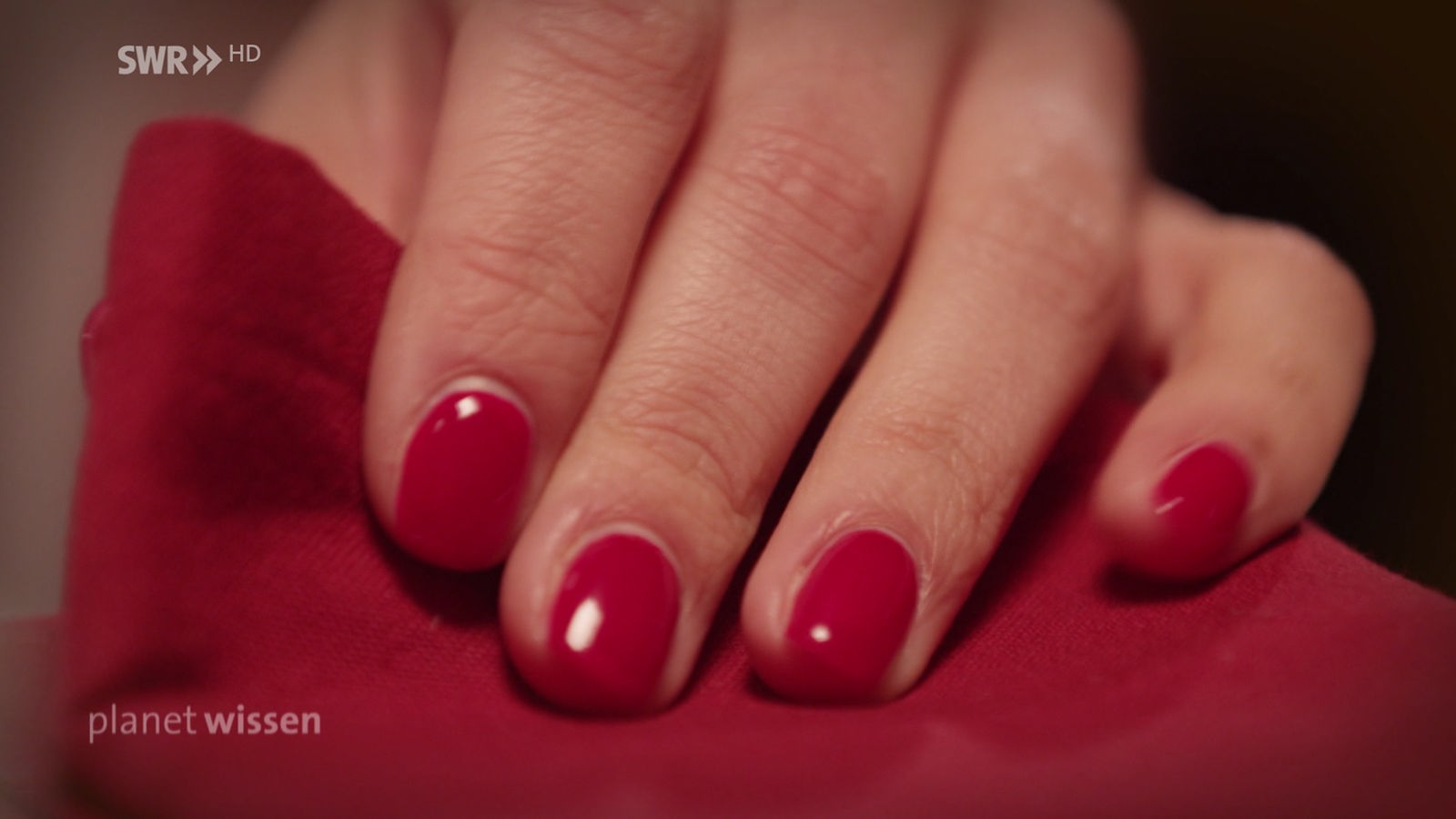 Eine Frauenhand mit rot lackierten Nägeln fassteine rote Stoffserviette.