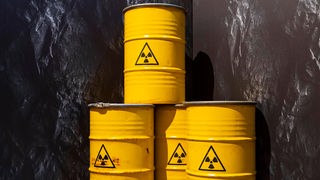 Vier gelbe Fässer mit radioaktivem Abfall stehen vor dunklem Hintergrund.
