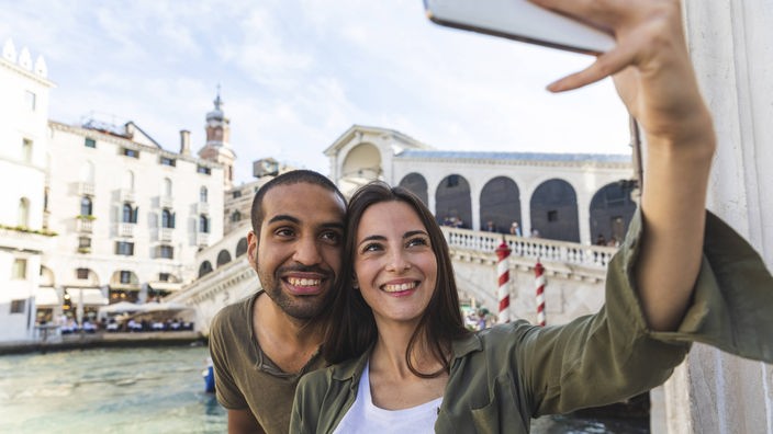 Eine Frau und ein Mann machen ein Selfie vor der Rialtobrücke in Venedig