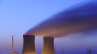 Die beleuchteten und rauchenden Schornsteine eines Atomkraftwerkes in der Abenddämmerung