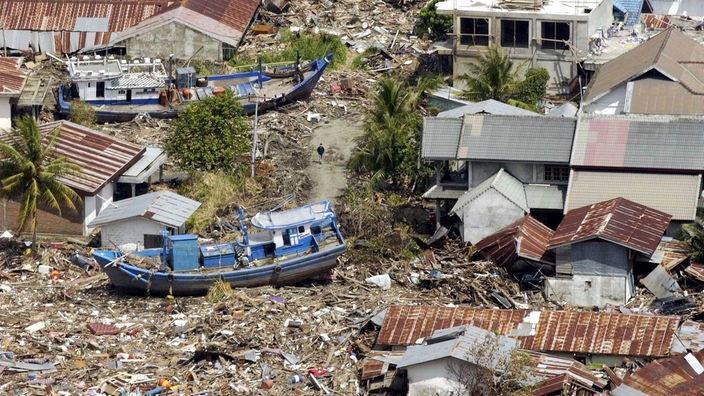 Zerstörte Häuser und Schiffe nach einem Tsunami. 