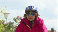 Eine Frau mit Helm und Sonnenbrille radelt auf die Kamera zu.