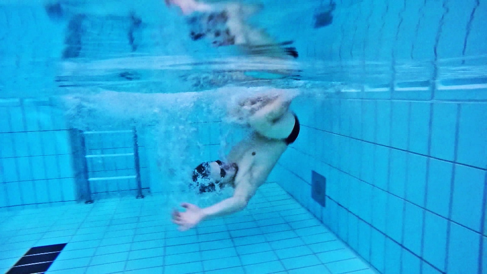 Unterwasseraufnahme: Schwimmer bei einer Rollwende im Schwimmbecken.