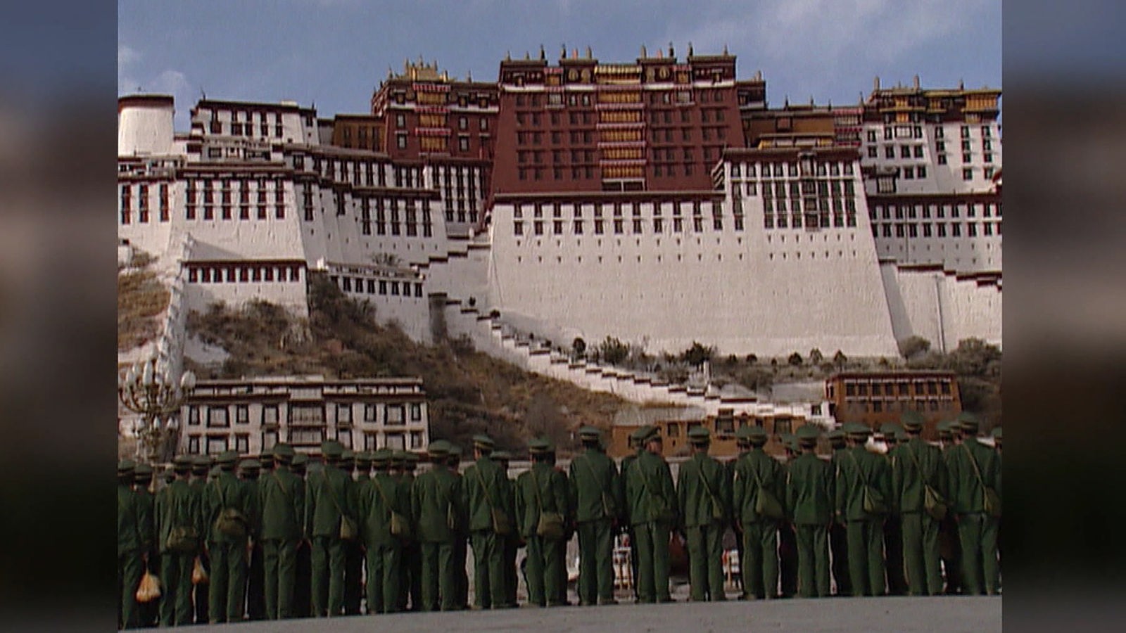 Uniformierte Chinesen stehen auf einem Platz. Im Hintergrund sieht man erhöht den Potala-Palast.
