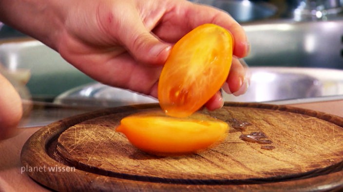 Eine gelbe Tomate wird auf einem Holzbrett halbiert.