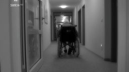 Pflegeheim mit einer Seniorin im Rollstuhl allein auf einem Flur.