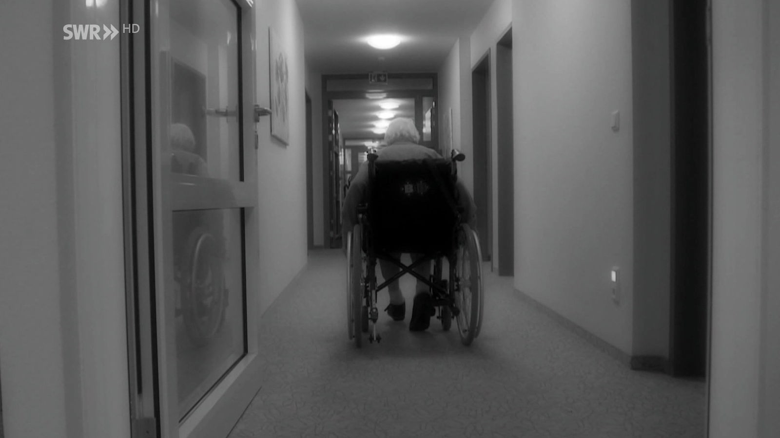 Pflegeheim mit einer Seniorin im Rollstuhl allein auf einem Flur.