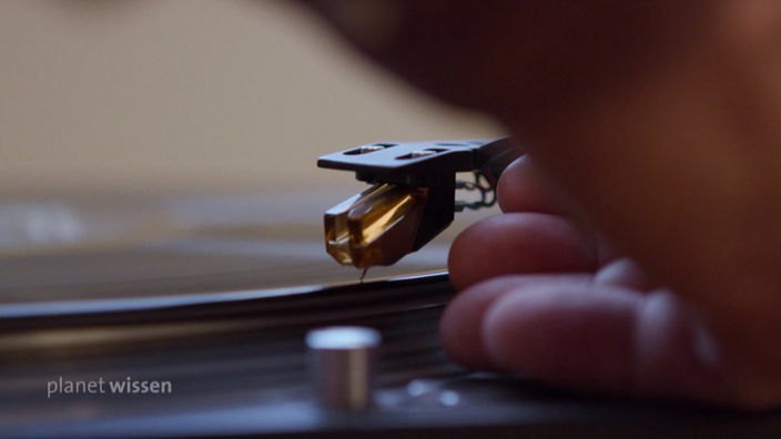 Eine Hand legt die Nadel eines Schallplattenspielers auf eine Schallplatte vorsichtig ab.
