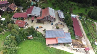 Luftaufnahme eines landwirtschaftlichen Hofgemeinschaft mit mehreren Gebäuden, Ställen und Wiesen.