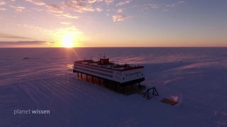 Die Forschungsstation Neumayer III in der Weite der Antarktis mit untergehender Sonne.