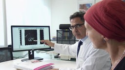 Eine Frau mit rotem Kopftuch bekommt von ihrem Arzt ihre Mammographie am Monitor erläutert.