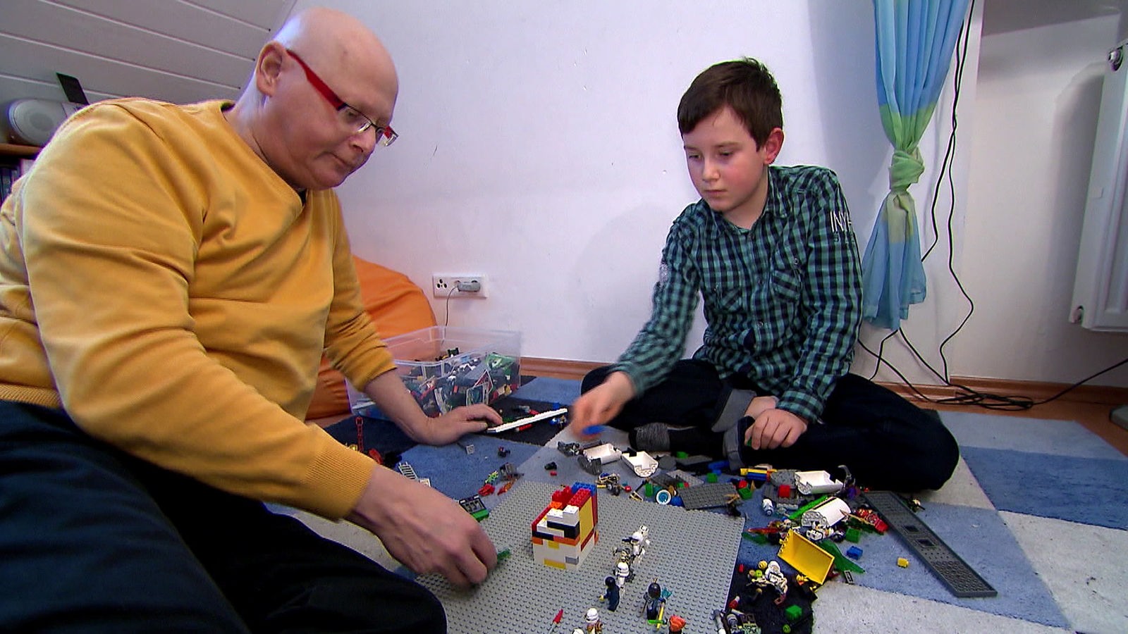 Vater und Sohn spielen Lego auf einem Teppichboden.