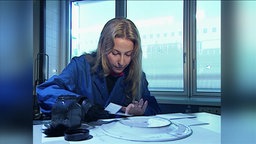 Eine Frau im Labor nimmt Fingerabdrücke von einem großen Teller ab.