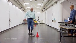Ein älterer Mann läuft in einem Messlabor um eine rote kleine Pylone am Boden.