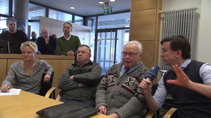 Mehrere Menschen sitzen mit einem ARD-Reporter an einem Tisch.
