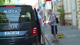 Zwei Männer stehen an einem VW-Bus mit offener Tür.