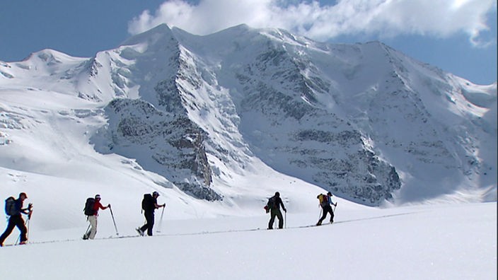Bergwanderer im Schnee vor einer beeindruckenden Bergwand im Sonnenschein.
