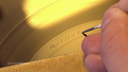 Hand mit spitzer Nadel ritzt Zahlen auf eine 'goldene' Lackfolie, die als Vorlage für die Druckmatrizen dient.