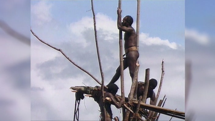 Männer des Sa-Volkes stehen auf einem hölzernen Gerüst.