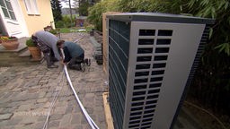 Zwei Techniker verlegen die Kabel für eine Wärmepumpe vor einem Haus.