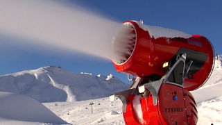 Rote Schneekanone sprüht Kunstschnee in verschneiter Bergatmosphäre.