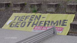 Banner an einem gepflasterten Hang mit der Aufschrift 'Tiefen-Geothermie wollen wir nicht'.
