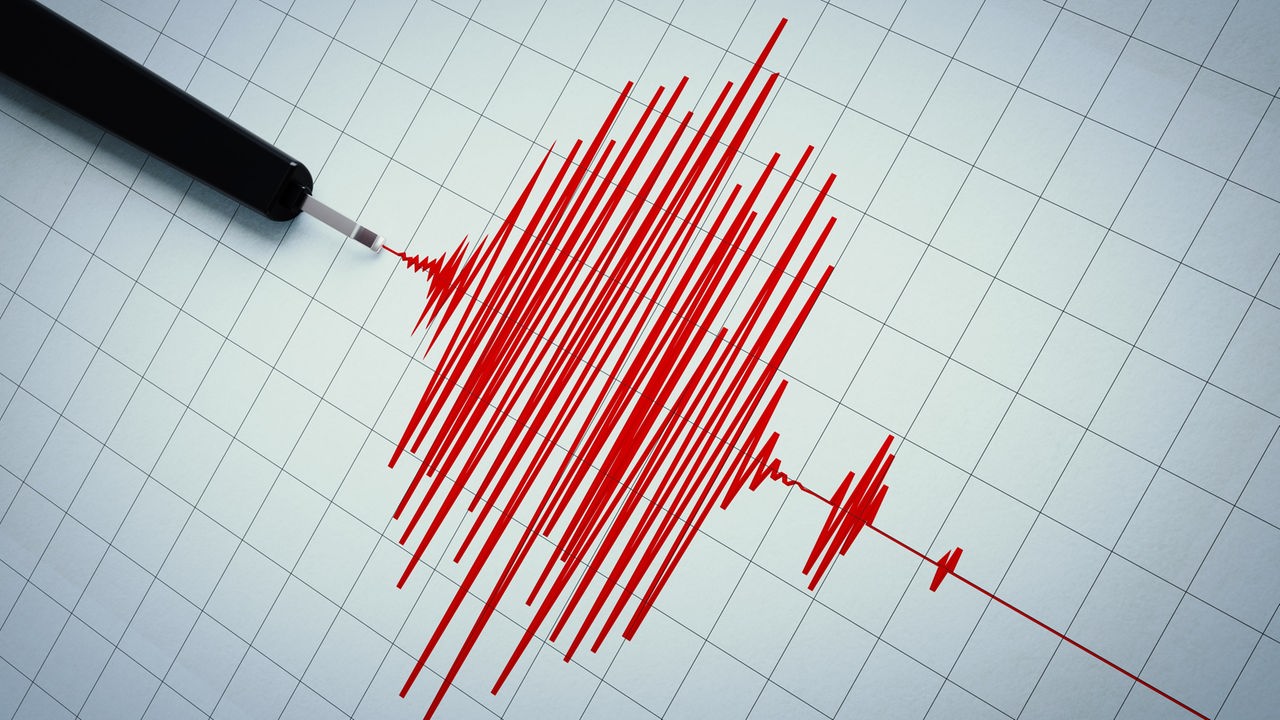 Ein Erdbebenschreiber, der mit großen, roten Amplituden ein Erdebebenstoß aufs Papier zeichnet. 