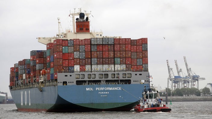Ein riesiges Containerschiff wird von einem kleinen Schlepper gezogen