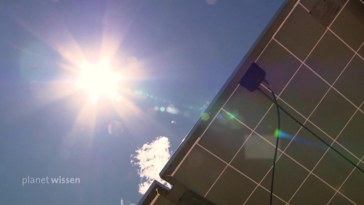 Blick von unten auf ein Solarpanel mit darüber einer strahlenden Sonne am blauen Himmel.