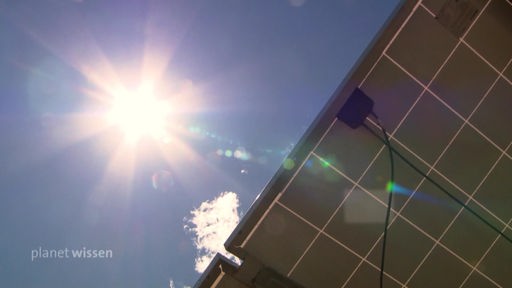 Blick von unten auf ein Solarpanel mit darüber einer strahlenden Sonne am blauen Himmel.