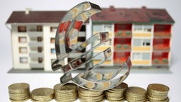 Überdimensionales Euro-Symbol steht auf Münzen vor Mietshäusern 