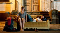 Zwei Frauen und Couchsurferinnen sitzen mitten auf einer Straße auf einer Couch