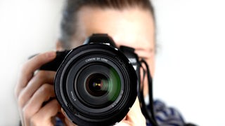 Ein Fotograf hält eine Spiegelreflexkamera in seinen Händen.