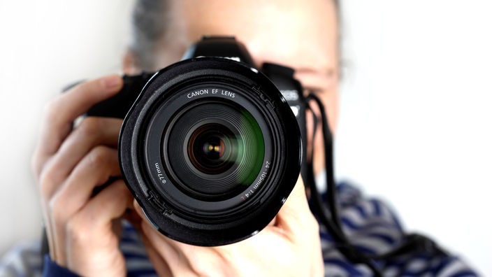 Ein Fotograf hält eine Spiegelreflexkamera in seinen Händen.
