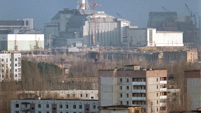 Die leerstehenden Wohnhäuser in der nahen Umgebung des Unglücksreaktors Tschernobyl. Im Hintergrund ist der einbetonierte Reaktor zu sehen, ein Schornstein ragt in den Himmel