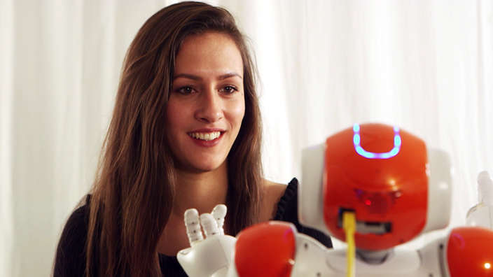 Eine Frau sitzt vor einem Tisch, auf dem ein kleiner Roboter sitzt .