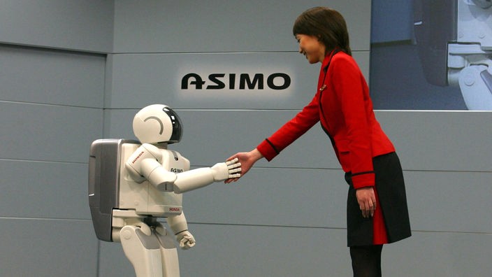 Ein humaoider Roboter gibt einer Frau die Hand.