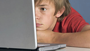 Ein Junge sitzt am Tisch und schaut auf den Bildschirm seines Laptops.