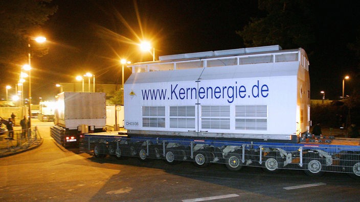 Ein großer, scheunenartiger Transportbehälter, in dem ein Castor transportiert wird. Auf dem weißlackierten Behälter steht in blauer Schrift www.Kernenergie.de