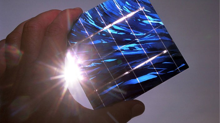 Gegenlichtaufnahme einer Solarzelle, die von einer Hand gegen die Sonne gehalten wird