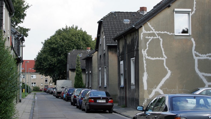 Straße mit einem Haus, dessen Mauer von mehreren Rissen durchzogen ist