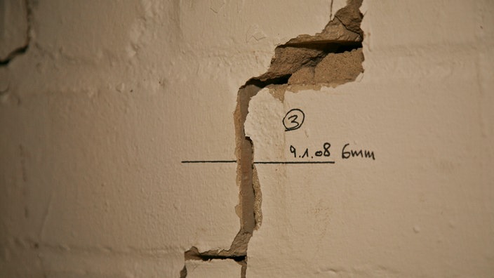 Riss in einer weiß getünchten Wand. Rechts neben dem Riss ist mit Filzstift die Aufschrift '6 mm' geschrieben. | Bildquelle: VBHG Riss in einer weiß getünchten Wand. Rechts neben dem Riss ist mit Filzstift die Aufschrift '6 mm' geschrieben.