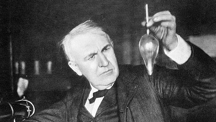 Thomas Alva Edison hält eine Glühbirne.