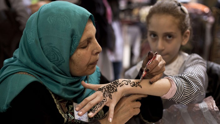 Eine Orientalin bemalt einem Mädchen die Handfläche mit Henna
