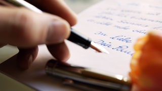 Hand schreibt mit Füller auf Papier