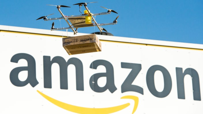 Eine Drohne mit einem Amazon-Paket fliegt am Amazon-Logistikzentrum Leipzig vorbei