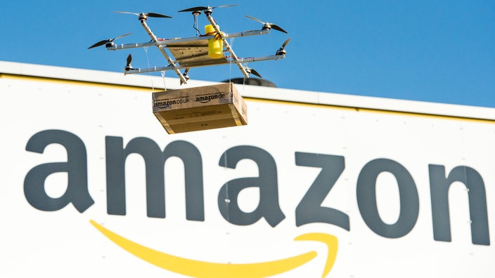 Eine Drohne mit einem Amazon-Paket fliegt am Amazon-Logistikzentrum Leipzig vorbei | Bildquelle: dpa Eine Drohne mit einem Amazon-Paket fliegt am Amazon-Logistikzentrum Leipzig vorbei