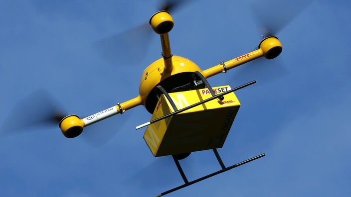 Der gelbe DHL-Paketkopter fliegt mit einem Paket durch die Luft