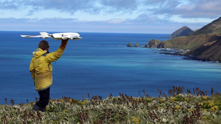 Mann steht an einer Klippe über dem Meer und lässt ein Modellflugzeug starten